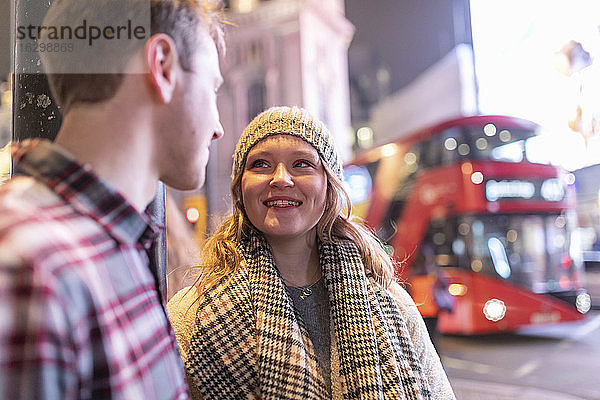Junges Paar im Gespräch am Piccadilly Circus mit Doppeldeckerbus im Hintergrund