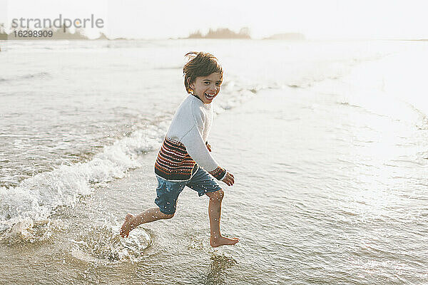 Fröhlicher Junge läuft im Wasser am Strand