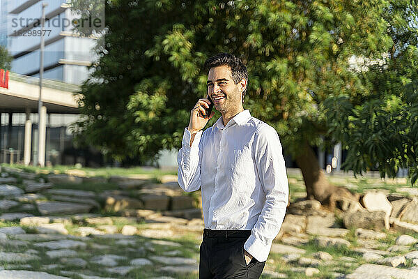Lächelnde männliche Fachkraft  die über ein Smartphone spricht  während sie im Park steht