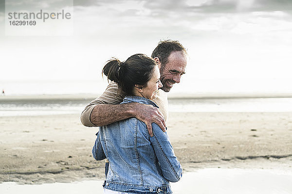 Fröhliches reifes Paar steht am Strand gegen den Himmel am Wochenende