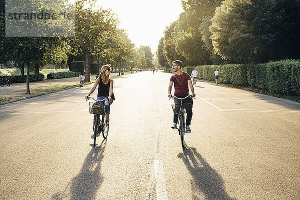 Glückliches Paar Radfahren auf der Straße inmitten von Bäumen im Park bei Sonnenuntergang
