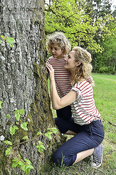Mutter und Tochter betrachten die Rinde eines Baumes im Wald