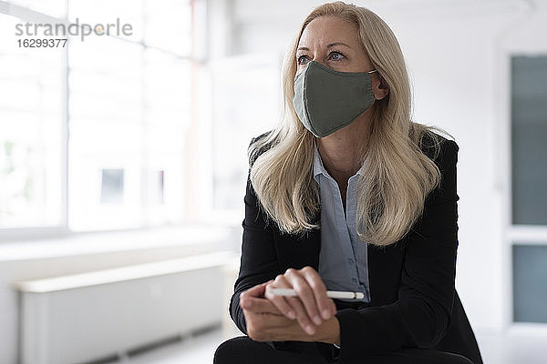 Geschäftsfrau mit Gesichtsmaske  die wegschaut  während sie im Büro zu Hause steht