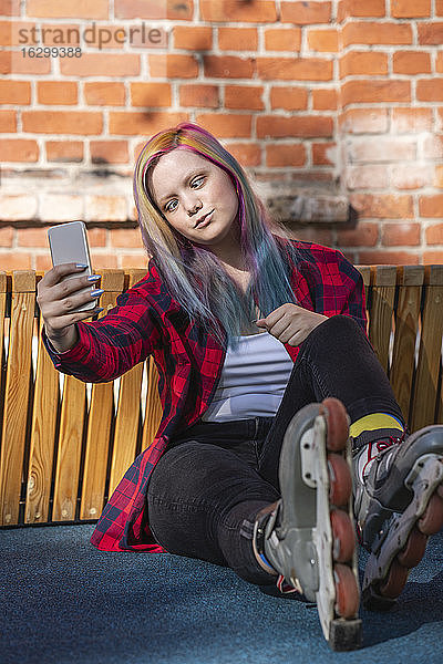 Junge Frau mit gefärbten Haaren und Rollschuhen  die ein Selfie mit ihrem Smartphone macht  mit schiefem Blick