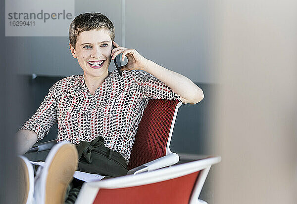 Glückliche Geschäftsfrau  die auf einem Bürostuhl sitzt und telefoniert