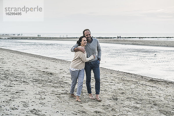 Glückliches Paar  das sich umarmt  während es am Strand bei Sonnenuntergang spazieren geht
