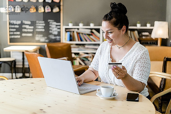 Glückliche junge Frau beim Online-Shopping am Laptop in einem Café
