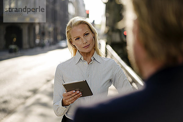 Selbstbewusste Unternehmerin  die ein digitales Tablet hält  während sie einen Geschäftsmann ansieht und in der Stadt diskutiert
