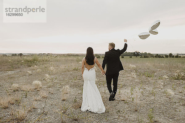 Braut und Bräutigam mit Herzform Ballons zu Fuß gegen den Himmel