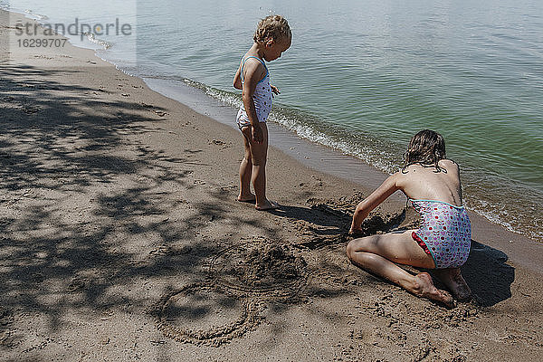 Junge Mädchen spielen im Sand während der Sommerferien am Strand