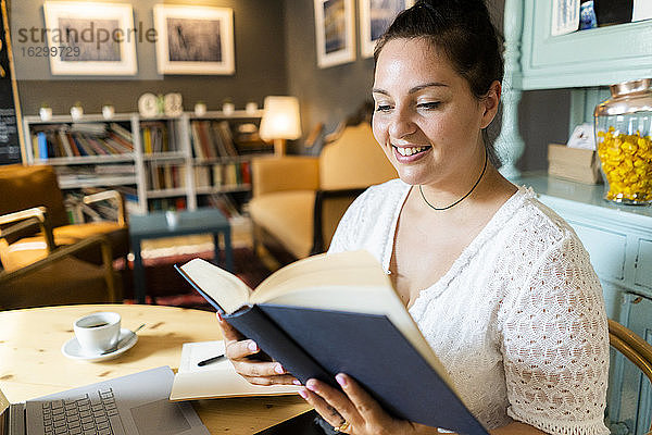 Lächelnde üppige Frau  die ein Buch liest  während sie am Tisch im Restaurant sitzt