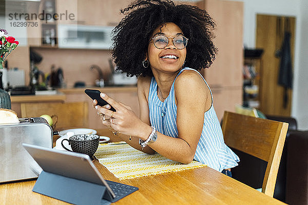 Junge Geschäftsfrau  die ein Mobiltelefon benutzt  während sie am Schreibtisch im Heimbüro sitzt