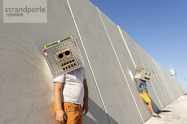 Jungen mit Robotermasken stehen an einer Mauer in der Stadt an einem sonnigen Tag