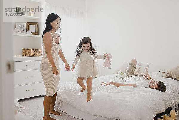 Lächelnde Eltern schauen auf ihre Tochter  die zu Hause auf dem Bett steht