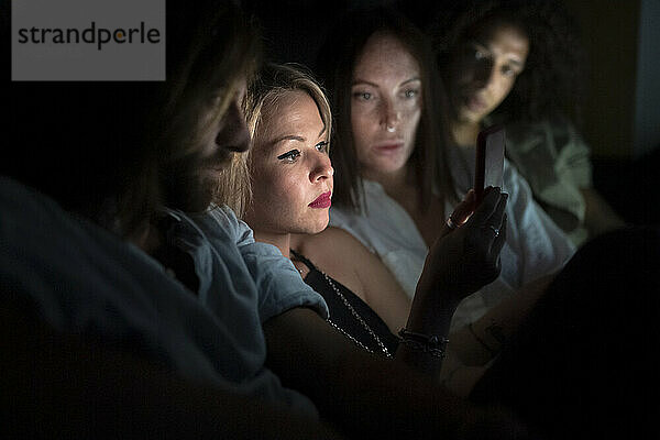 Männliche und weibliche Freunde schauen in der Nacht auf ihr Smartphone