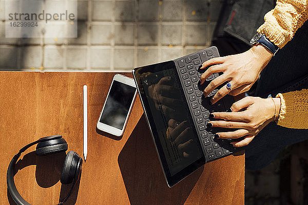 Hände einer Studentin  die auf einer digitalen Tablet-Tastatur tippt  während sie in einem Straßencafé in der Stadt sitzt
