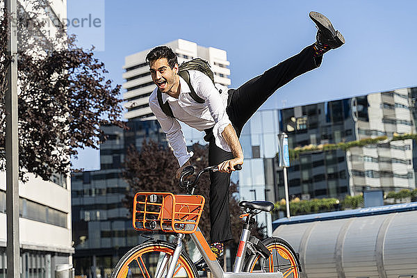 Fröhlicher Geschäftsmann bei einem Stunt auf einem Elektrofahrrad in der Stadt