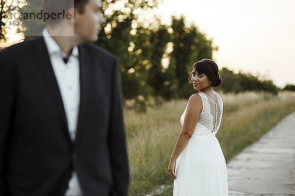 Junge Braut schaut Bräutigam an  während sie bei Sonnenuntergang auf dem Fußweg steht