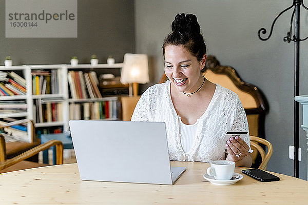 Glückliche  üppige junge Frau beim Online-Shopping am Laptop in einem Café