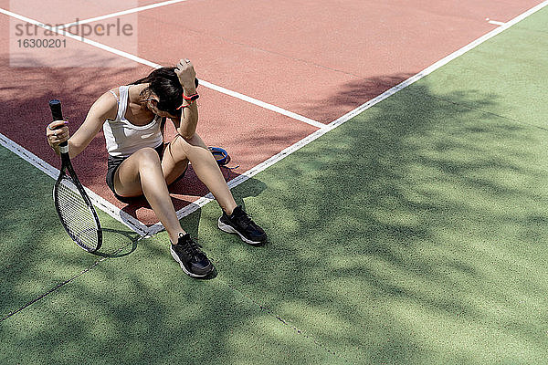 Traurige Tennisspielerin sitzt auf dem Boden eines Sportplatzes