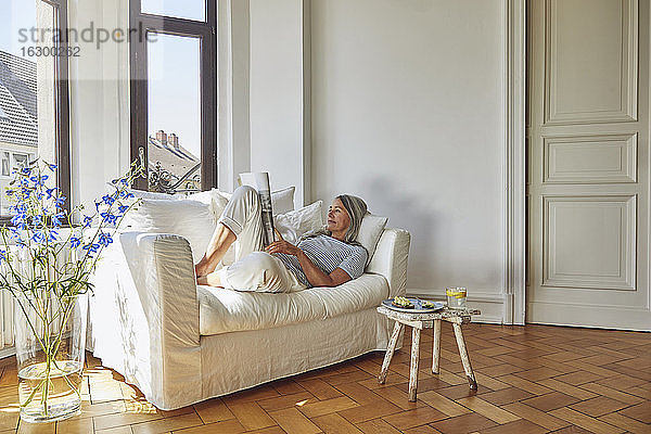 Frau liest Zeitschrift über Sofa im Wohnzimmer