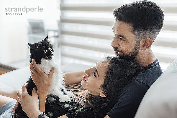 Ehepaar teilt Zärtlichkeit mit Katze  während es zu Hause sitzt