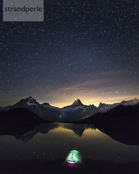 Sternenhimmel über dem beleuchteten Zelt am Ufer des Bachalpsees bei Nacht