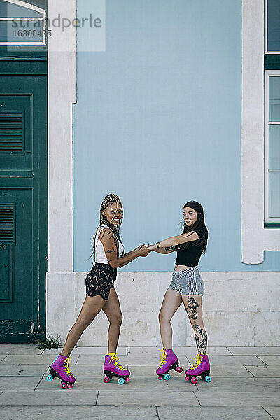 Freunde halten sich an den Händen  während sie auf dem Fußweg an der Mauer in der Stadt Rollschuh laufen