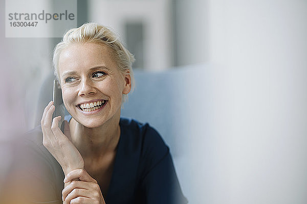 Nahaufnahme einer fröhlichen Geschäftsfrau  die über ein Smartphone spricht  während sie im Büro sitzt