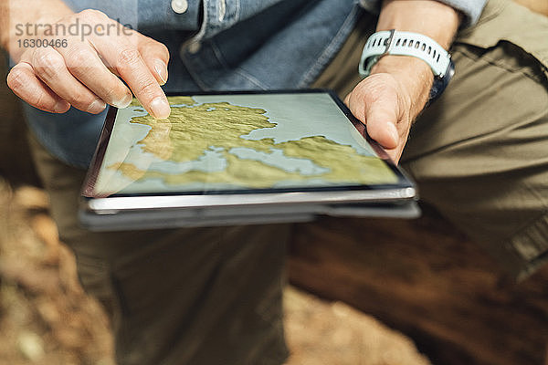 Nahaufnahme der Hände eines Mannes  der eine Karte über einem digitalen Tablet im Wald benutzt