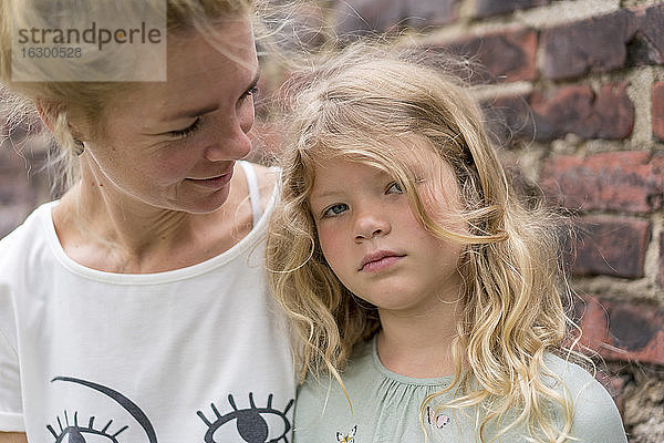 Blondes Mädchen mit Mutter gegen Backsteinmauer im Hinterhof