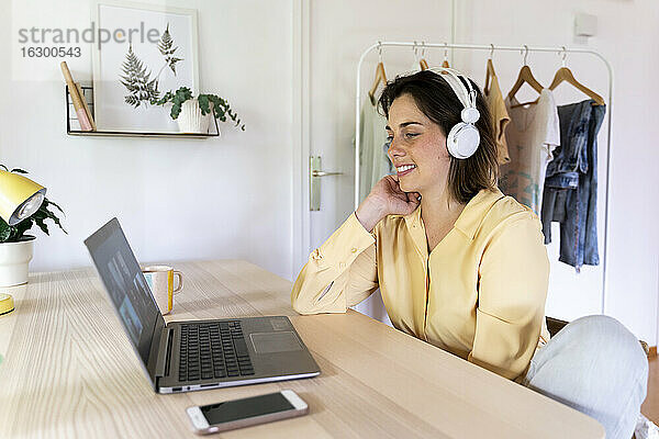 Glückliche junge Frau genießt Videoanruf mit Freunden durch Laptop zu Hause