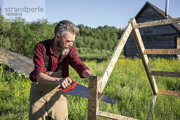 Zimmermann sägt Bretter beim Bau eines Spielhauses an einem sonnigen Tag