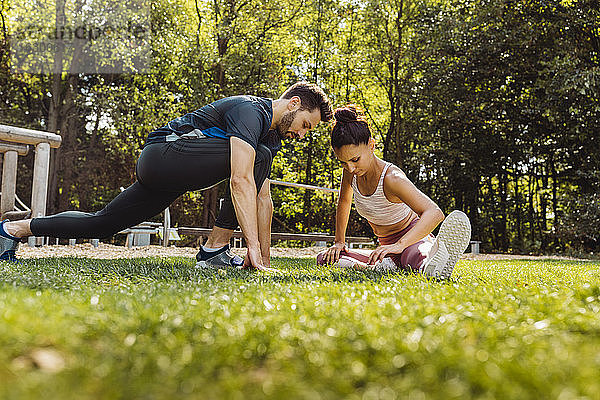 Mann und Frau dehnen sich im Gras in der Nähe eines Fitnessparcours
