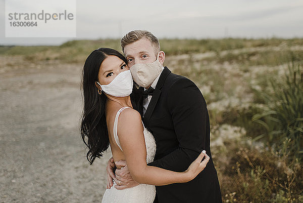 Braut mit Bräutigam mit Gesichtsschutzmaske im Feld während COVID-19