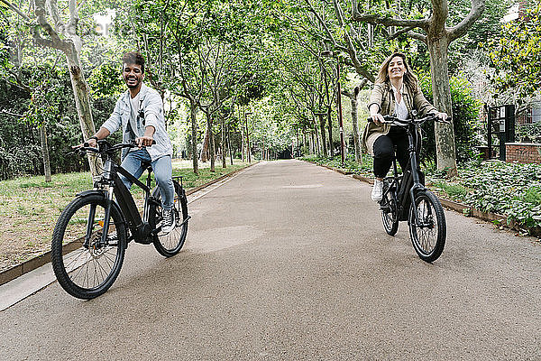 Glückliches junges Paar auf Elektrofahrrädern auf der Straße inmitten von Bäumen