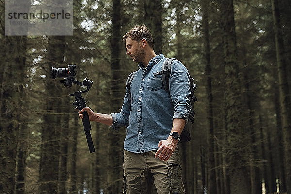 Mann filmt mit Kamera und Gimbal  während er gegen Bäume im Wald steht