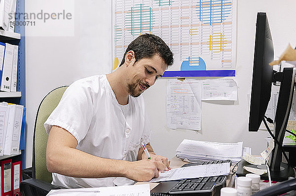 Männlicher Arzt schreibt am Schreibtisch in einer Apotheke an einem Dokument