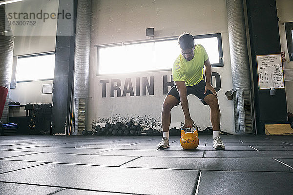 Männlicher Sportler hebt eine Kettlebell  während er im Fitnessstudio auf dem Boden steht