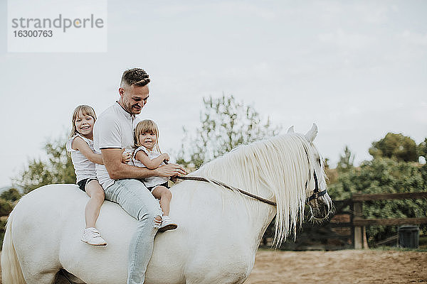 Vater mit Töchtern reitet Pferd in Scheune gegen Himmel