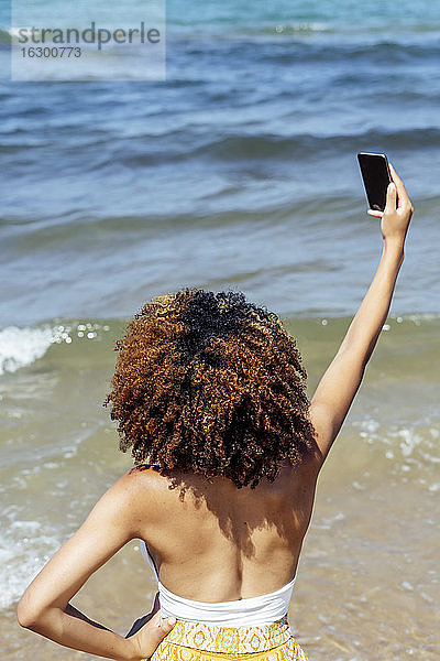 Junge Frau mit lockigem Haar  die ein Selfie macht  während sie im Sommer im Meer steht