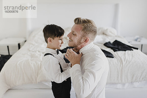 Lächelnder Vater und Sohn  die sich im Schlafzimmer für die Hochzeit anziehen
