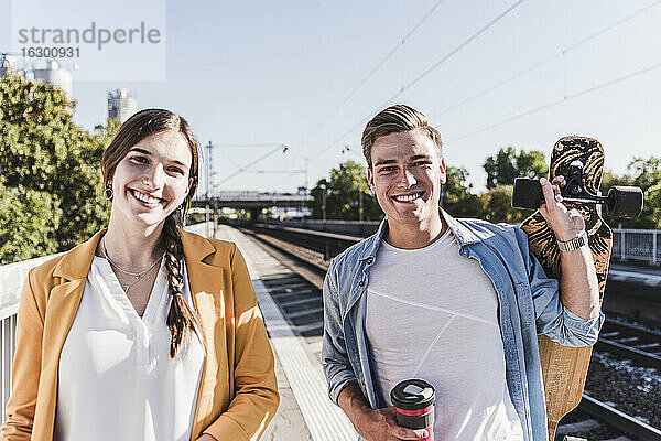 Lächelnde männliche und weibliche Freunde auf dem Bahnsteig eines Bahnhofs