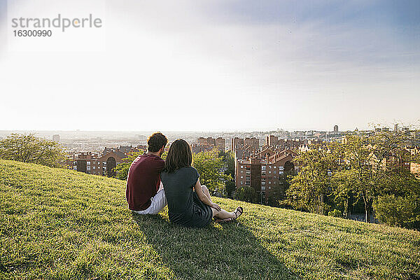 Paar bewundert Sonnenuntergang Blick auf die Stadt  während auf Gras sitzen
