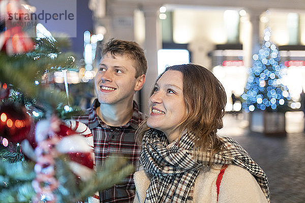 Glückliches junges Paar  das den Weihnachtsbaum und die Lichter betrachtet  während es in der Stadt steht