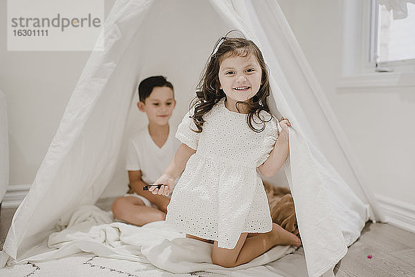 Lächelnde Schwester mit Bruder kniend im Zelt zu Hause