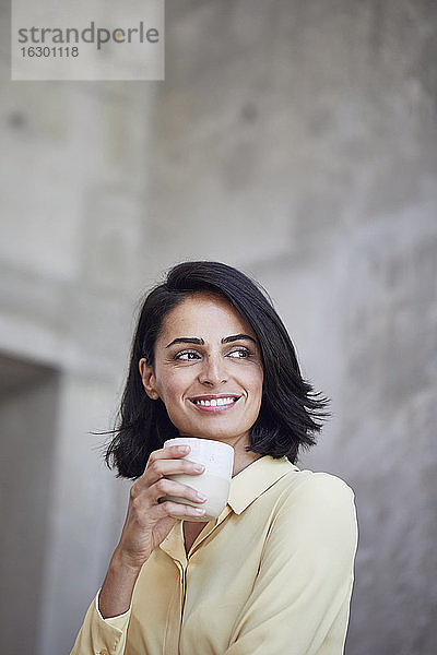 Nahaufnahme einer lächelnden Unternehmerin  die eine Kaffeetasse an die Wand eines Büros hält