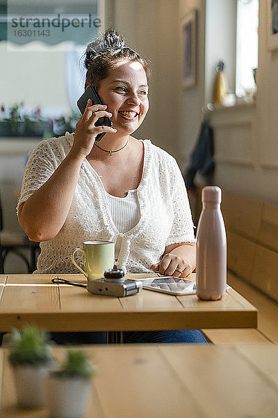 Üppige junge Frau  die am Tisch in einem Restaurant sitzt und über ein Mobiltelefon spricht