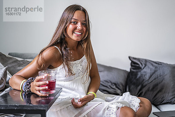 Lächelnde Frau mit Getränk auf der Couch zu Hause sitzend