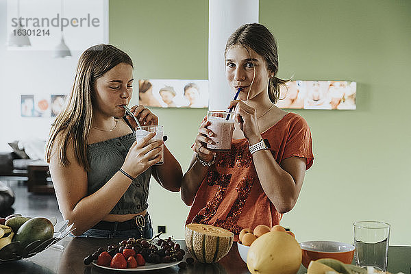 Teenager-Mädchen stehen in der Küche und trinken frische Frucht-Smoothies mit Trinkhalmen